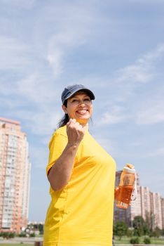 Sport and fitness. Senior sport. Active seniors. Excited senior woman drinking water after workout outdoors on the sports ground