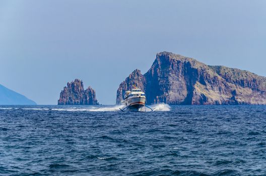 Ferry catamaran covering the route between the islands of Stromboli and Panarea in the Tyrrhenian Sea and two large cliffs behind it