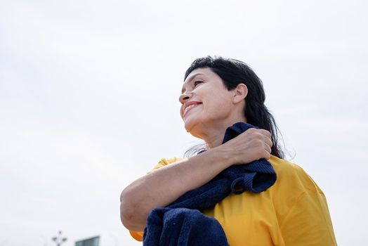 Sport and fitness. Senior sport. Active seniors. Smiling senior woman wiping out sweat after hard workout outdoors on sky background