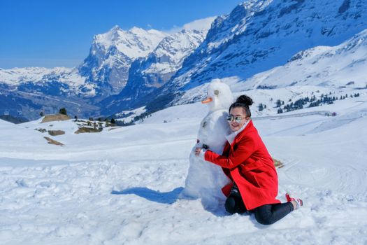 Beautiful woman hugging snowman in red coat outdoors