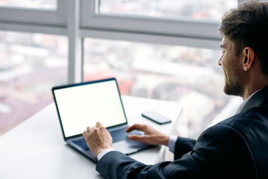 A man is typing text on a laptop in the office and a mobile phone on the table