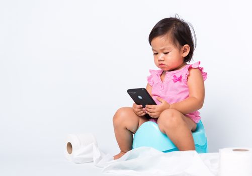 Asian little cute baby child girl education training to sitting on blue chamber pot or potty and play smart mobile phone with toilet paper rolls, studio shot isolated on white background, wc toilet