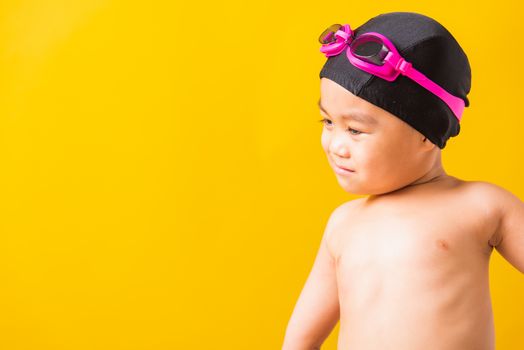 Summer vacation concept, Closeup portrait Asian happy cute little child boy wearing goggles and swimsuit, Kid having fun with in summer vacation looking side, studio shot isolated yellow background