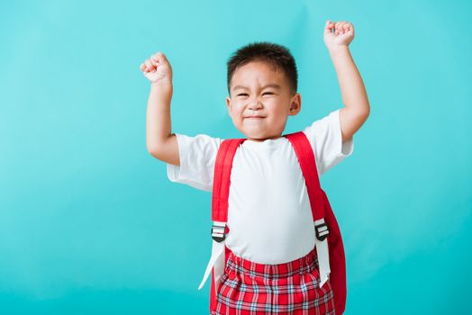 Back to school. Portrait happy Asian cute little child boy in uniform smile raise hands up glad when go back to school, isolated blue background. Kid from preschool kindergarten with school backpack