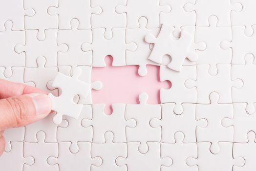 Top view flat lay of hand-holding last piece white paper jigsaw puzzle game last pieces put to place for solve problem complete mission, studio shot on a pink background, quiz calculation concept