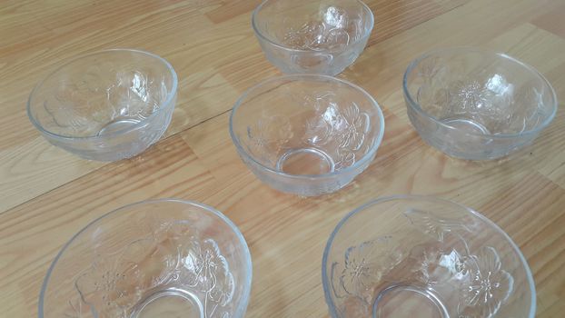 Top view of empty white glass bowls on a wooden floor. Glass bowl with flowers made on its wall