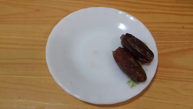 Close up view of fresh dried date palm served in ceramic small white plate over a wooden floor