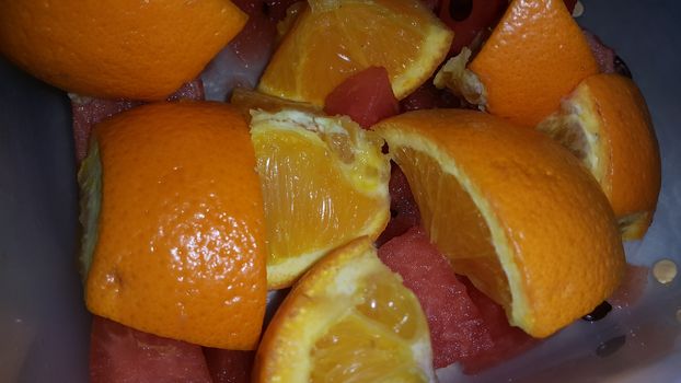 Closeup view of mixed fruits slices of oranges and red water melon served in a ceramic white plate. Water melon is sweet while oranges are citrus in taste