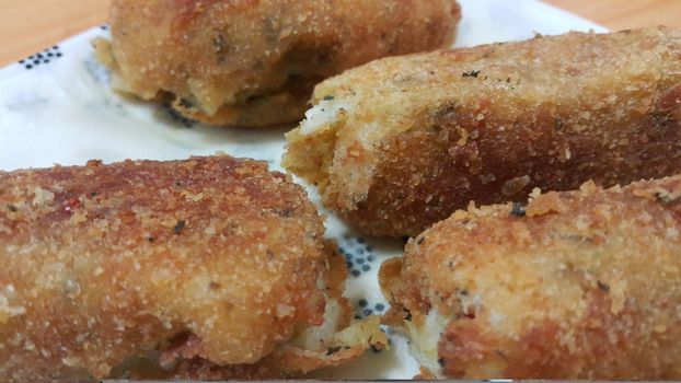 Closeup perspective view of home made spicy and delicious croquettes served in ceramic plate over wooden floor