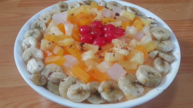 Creamy tasty sweet fruit trifle over custard with banana slices layered on surface on wooden floor. A top view of home made fruit trifle, a products for dessert after meal.