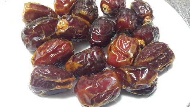 Close up view of fresh dried date palm served in ceramic small white plate over a wooden floor