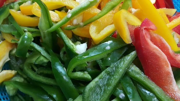 Closeup perspective view of slices of colorful green, yellow, red, purple hot shiny Shimla chilli or peppers.