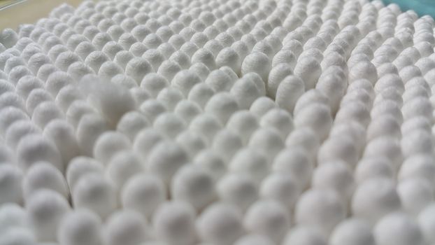Closeup view of several cotton buds heads arranged in rows and columns. The cotton buds consist of one small wad of cotton wrapped around one or both ends of a short rod made of wood or plastic.
