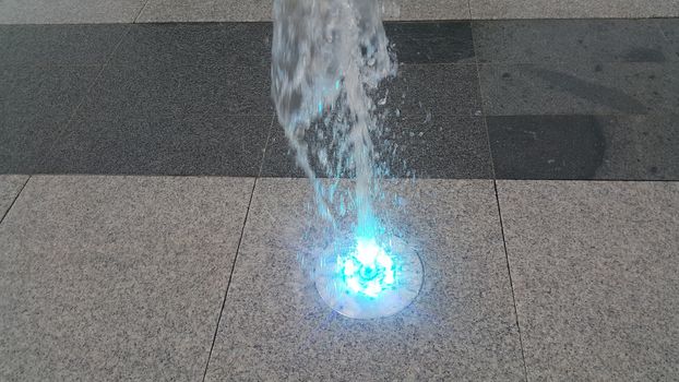 Beautiful and colorful light water fountain over concrete floor. Colorful water shape on fountain with grey background.
