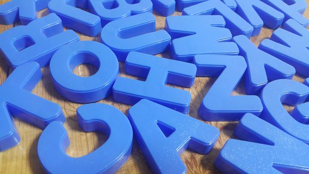 Set of plastic alphabet letters placed on a wooden floor. Alphabet set is used for educating children to learn words and language