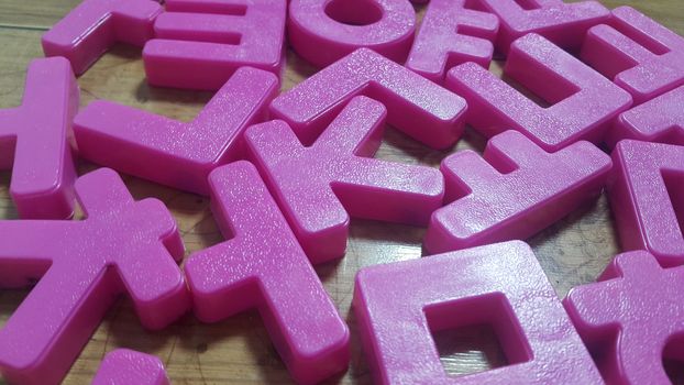 Set of plastic alphabet letters placed on a wooden floor. Alphabet set is used for educating children to learn words and language