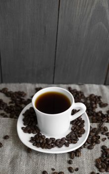 Coffee cup with roasted coffee beans on wooden table background. Mug of black coffe with scattered coffee beans on a wooden table. Fresh coffee beans