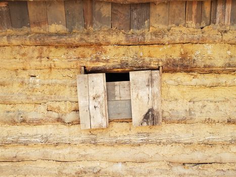 boarded window on old log and mud cabin building