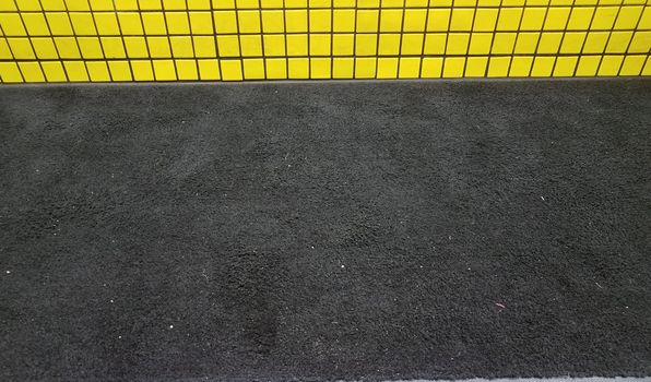 dirty black carpet or rug with yellow tiles on wall