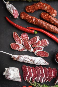 Set of various spanish dry cured salami sausages slices and whole cuts on black textured background.