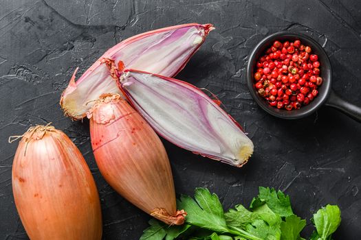 Organic shallot, bio eschalot or farm scallion raw ripe onions with greens and rose peppercorns sliced and halved black concrete textured background top view.