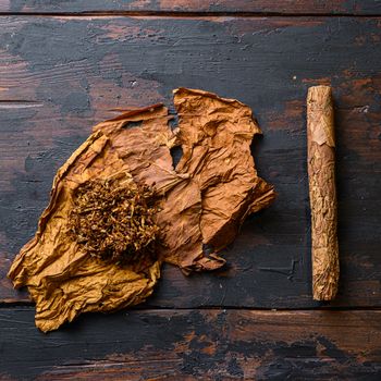 Cut tobacco and tobacco leaves with cigar on wood background on vintage dark table. overhead shot top view .