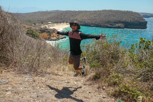 A young man is jumping on the beach, Having fun, Summer vacation holiday lifestyle. Happy teenager jumping freedom. Asian guy in shorts and a T-shirt jumping on a cliff.