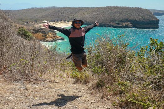 Man jumping cliff against sea with blue sky. A young man is jumping on the beach, Having fun, Summer vacation holiday lifestyle. Happy teenager jumping freedom. Asian guy in shorts and a T-shirt.