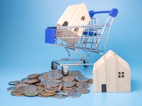 A model wooden house on a shopping cart With a pile of coins On a blue background. Mortgage concept. Money and house.


