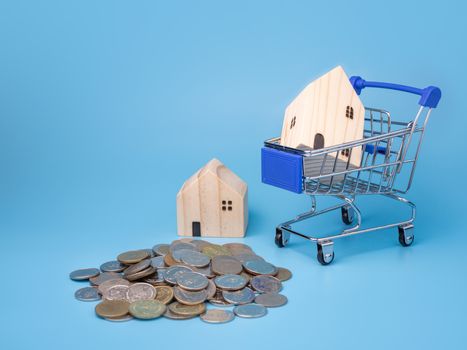 A model wooden house on a shopping cart With a pile of coins On a blue background. Mortgage concept. Money and house.