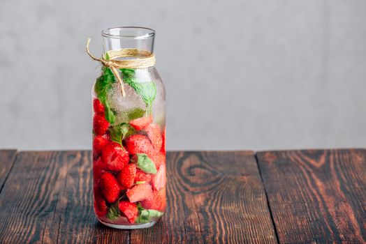 Bottle of Water Flavored with Fresh Strawberry and Basil Leaves on Wooden Table. Copy Space.