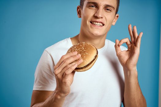 man with hamburger and white t-shirt blue background emotions gesturing with hands Copy Space. High quality photo