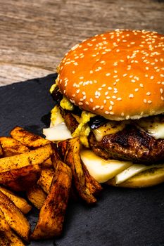 Homemade fresh tasty cheese burger and fried potatoes on a wooden table