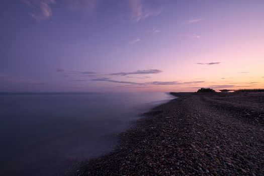 Sunset on a lonely beach, calm waters, small stones, long exposure, silk effect