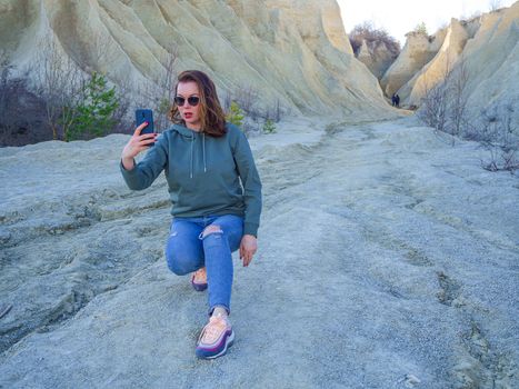 Hiker on mountain top with smartphone. Woman is standing and taking a picture on smartphone. Abandoned Quarry Of Rummu, Estonia. Scenic View Of Land Against Clear Blue Sky. Panoramic View.