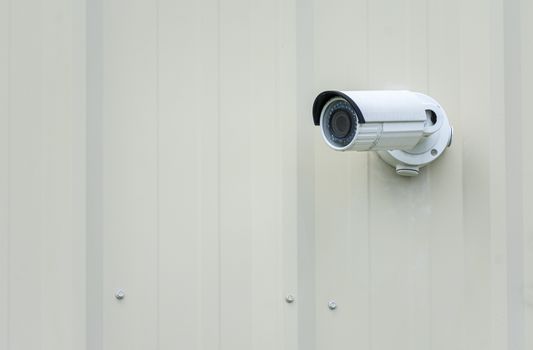 Horizontal shot of an outdoor security camera on a plain wall with copy space.

