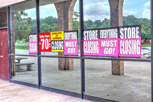 Horizontal shot of the windows of a retail store with going out of business signs posted on them after the pandemic