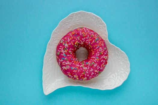 Donut with colorful sprinkles isolated lying on a white plate on blue background. Top view