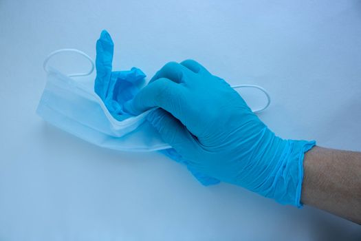 A man's hand in a blue latex glove holds a mask on a white background. Protect your hands and face from viruses