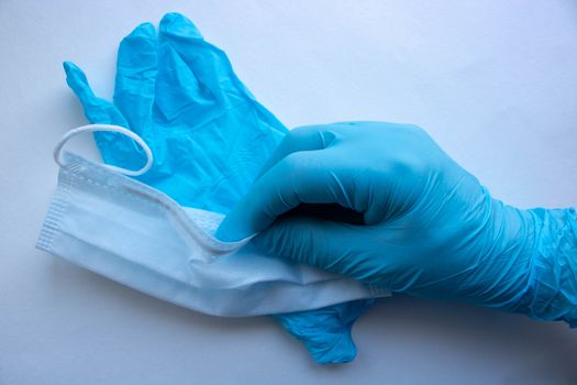 A man's hand in a blue latex glove holds a mask on a white background. Protect your hands and face from viruses