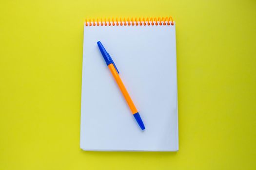 Notepad with an orange spiral and an orange pen, on a yellow background. top view copy space