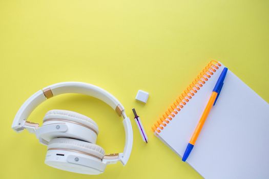 Modern white headphones next to a clean paper Notepad and pen on a yellow background. Musical concept. A copy of the space. The view from the top