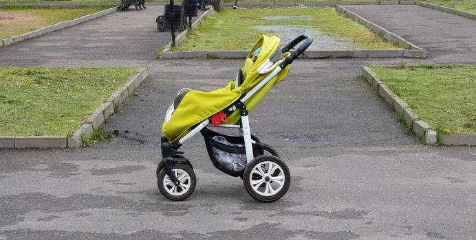 A green baby stroller stands in the middle of the Park. Travel with a child, transport a child, concepts of a child's walk.
