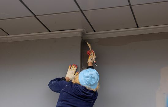 A Builder paints the facade of a gray house with a brush