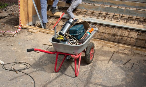 A close-up view shows a wheelbarrow loaded with construction tools. The concept of repair.