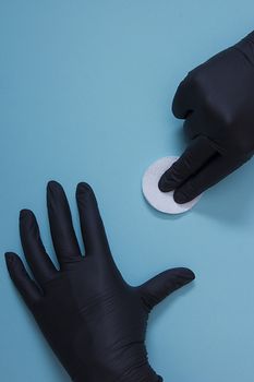 Hands in black nitrile gloves with a cotton sponge on a blue background