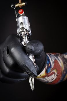 Tattoo machine in artist’s hand isolated on black background