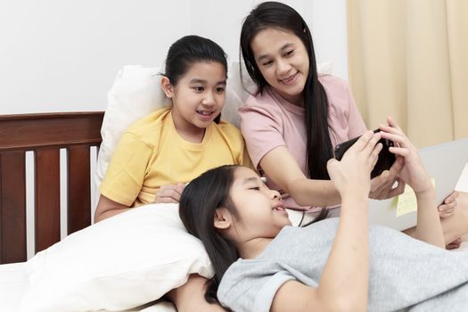 Asian family enjoy and relax on bed in bedroom. mother and daughters enjoy using laptop, tablet and smart phone together on bed.  Family concept.