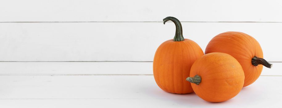 Three small pumpkins on white wooden background