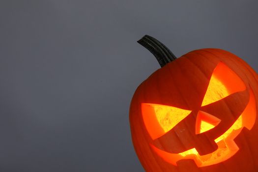 Funny glowing Halloween Jack O' Lantern Pumpkin on gray background